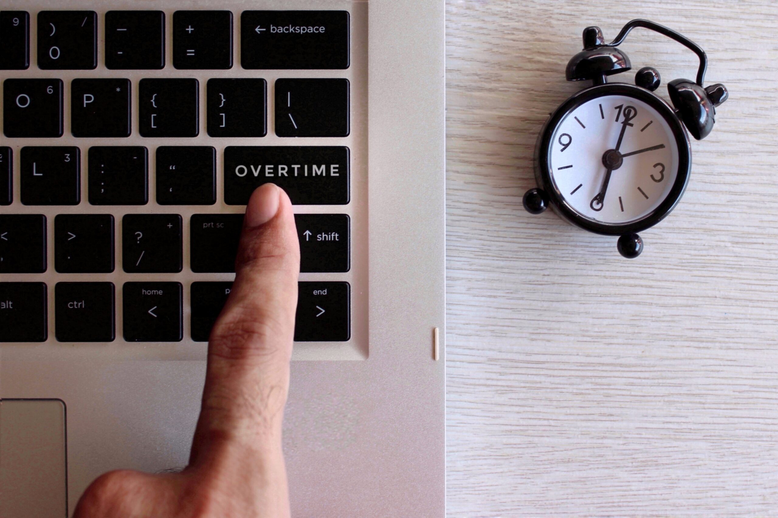 A hand over a laptop keyboard about to press a key labeled as overtime